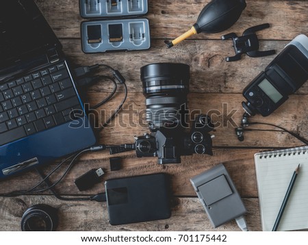 top view of work space photographer with digital camera, battery charger camera, memory card storage box, external harddisk, flash, computer laptop, notebook and camera accessory on wooden background