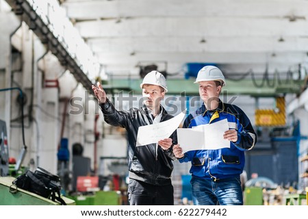 A young successful engineer discusses technical documentation with his help in the territory of a modern plant