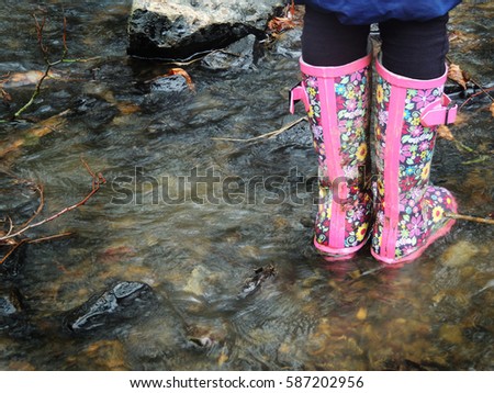 Child playing in river. Pink wellington boots.