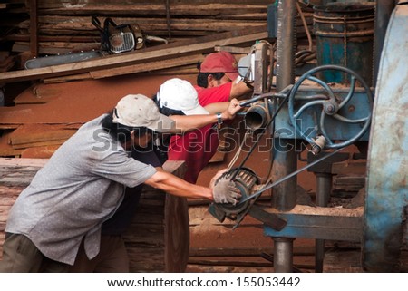 QUY NHON, VIET NAM, JUNE 18: Three woodworker try to pull cumbersome machine to split section of a tree trunk into plank at sawmill. June 18, 2012
