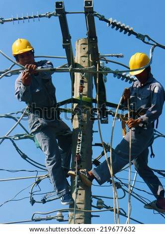 DONG THAP, VIET NAM- SEPT 23: Two Asian electrician climb high in pole to work, lineman with cable network, man repair electric post with belt safety, this is industry service, Vietnam, Sept 23, 2014