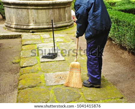 Sweeper, municipal cleaning worker sweeping autumn leaves in the garden