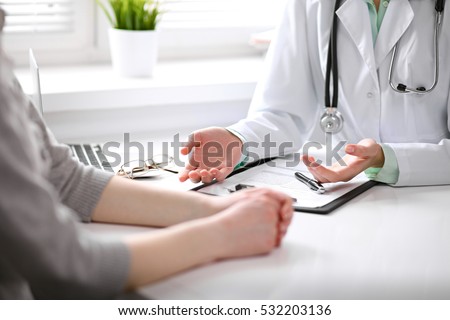 Close up of doctor and patient sitting at the desk near the window in hospital