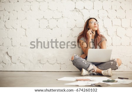 Wide shot of a freelance blog post writer working in a bright studio space sitting in a cafe or a campus surrounded by textile samples and fashion ilustrations
