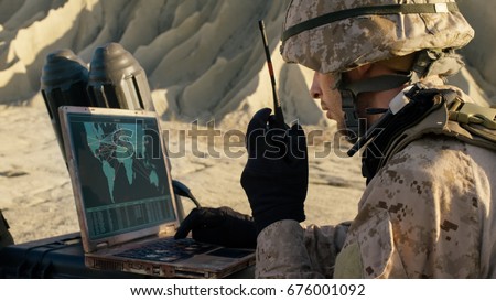 Soldier is Using Laptop Computer and Radio for Communication During Military Operation in the Desert.