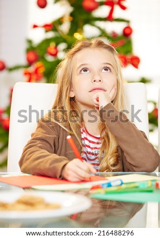 Pensive child writing wishlist to Santa Claus for christmas