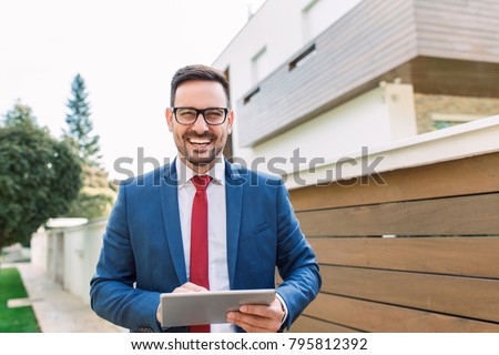 Smiling young salesman standing in front of the house
