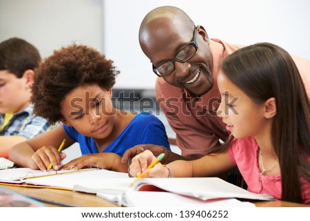 Teacher Helping Pupils Studying At Desks In Classroom