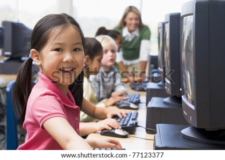 Children at computer terminals with teacher in background (depth of field/high key)