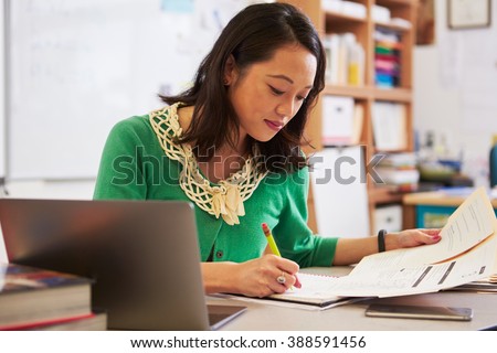 Female Asian teacher at her desk marking studentsâ?? work