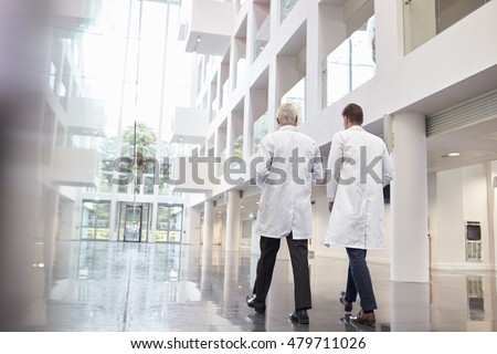 Rear View Of Doctors Talking As They Walk Through Hospital