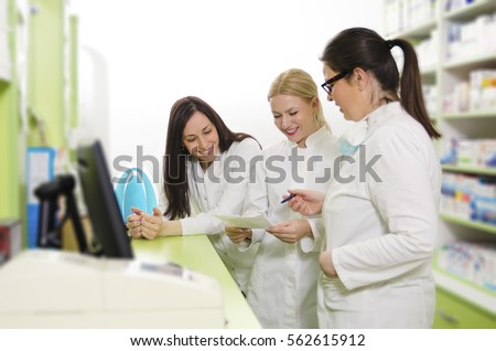 Three happy female pharmacists at work. looking at prescription, selective focus on last girl in row