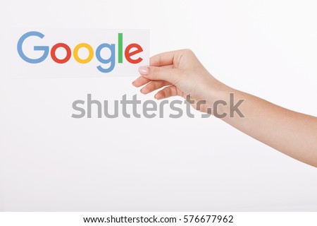 Kiev, Ukraine - August 22, 2016: Woman hands holding colorful Google logotype printed on paper on grey background. Google is USA multinational corporation.