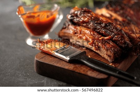 Delicious barbecued ribs seasoned with a spicy basting sauce and served with chopped fresh vegetables on an old rustic wooden chopping board in a country kitchen