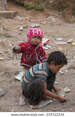HA GIANG, VIETNAM - NOV 14, 2014: Close up photo of unidentified poor Hmong child eating candy on the dirty ground in Dong Van rocky plateau. Dong Van rocky plateau is a well known geopark.