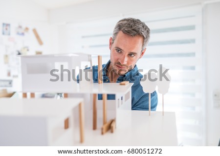 Handsome senior architect working on a construction project, he examines the model on which he works