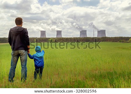 Pollution. Environmental problem. Father and his son looking on a emissions of plant. Factory chimneys (smoke stacks) polluting air on green field. Nuclear power plant. Ecology concept. Copy space.