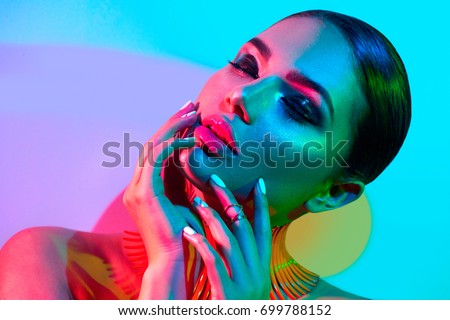 High Fashion model woman in colorful bright lights posing in studio, portrait of beautiful sexy girl with trendy make-up and manicure. Art design, colorful make up. Over colourful vivid background.