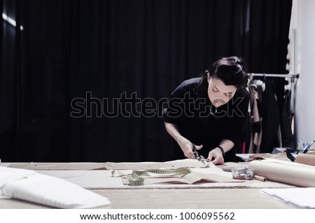 tailor cuts scissors, tailoring materials, professional female tailor using scissors and draft design cardboard on cloth material cut clothing design samples in production studio pattern table.
