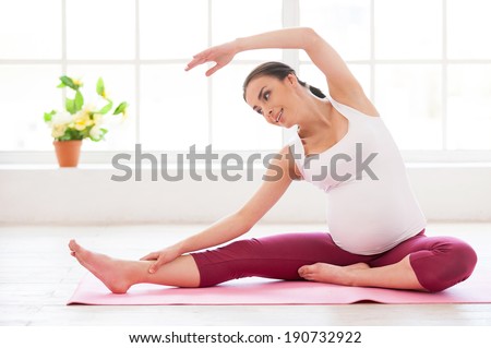 Pre-natal exercises. Beautiful pregnant woman exercising while sitting in lotus position