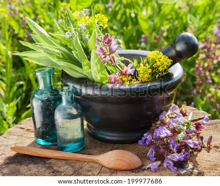 mortar with healing herbs and sage, glass bottle of essential oil outdoors