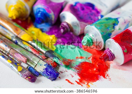 Tubes of multicolor oil paint and artist paintbrushes on canvas closeup.