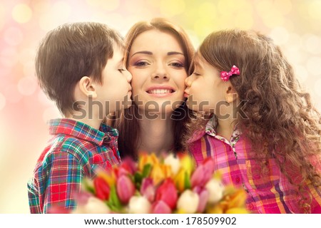 Portrait of children kissing her mother with flowers. Mother`s day concept. Family holiday