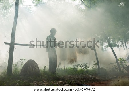 Bac Ninh, Vietnam - May 29, 2016: Fisherman mending fish net by Cau river under heavy smoke from discard rice straw fire