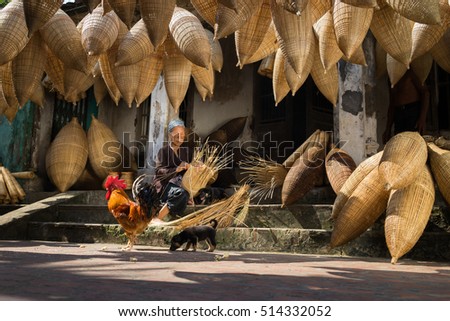 Hung Yen, Vietnam - July 9, 2016: Old house yard with many bamboo fish trap, a cock, and female craftsman making traditional bamboo fish trap at her old house in Thu Sy trade village
