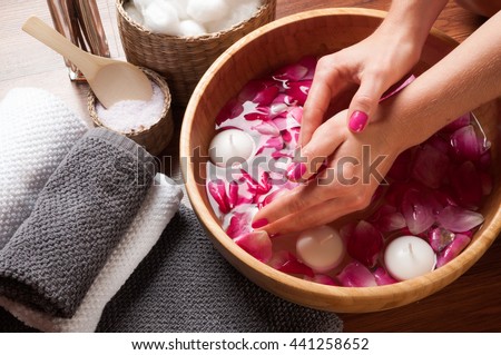 Female hands in bowl of spa water with flowers, hand care in nail salon, relaxing