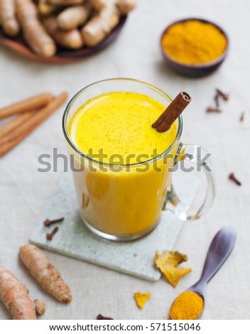 Turmeric drink, latte, tea, milk with cinnamon in a glass mug with fresh and dried turmeric on textile grey background.