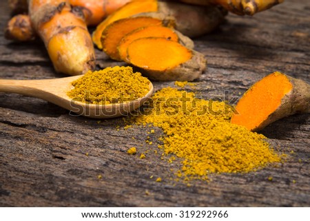 the turmeric powder in spoon and roots on wooden plate