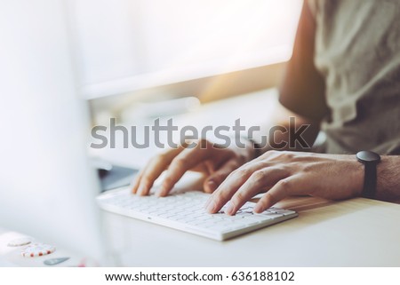 Young businessman working at sunny office on laptop, Man using desktop computer at home while sitting the wooden table