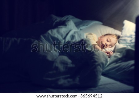 Cute little boy in yellow pyjamas is sweetly sleeping in bed with blue bed-clothes. Image with selective focus, toning and soft effects of shining light.