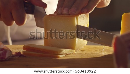 Super slow motion macro of a middle aged chef cutting cheese with knife on wooden board on restaurant kitchen table (extra close up)