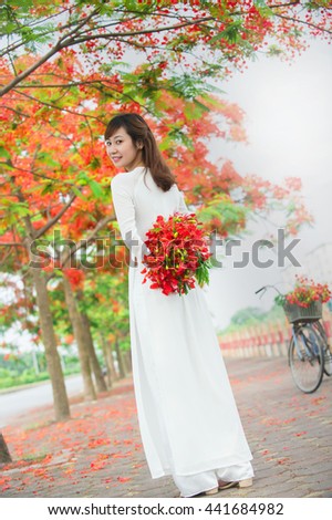 Hanoi, Vietnam, May 21th, 2016: Hanoi girl is charming in long-dress (the Ao dai - Vietnamese) and Royal Poinciana road (Delonix Regia). The Ao dai is traditional costume of Vietnamese woman.