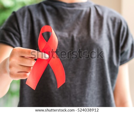 Red color ribbon awareness on young female woman girl teenager hand background: World aids day symbolic concept raising supportive help campaign public support people's health living with HIV, STD