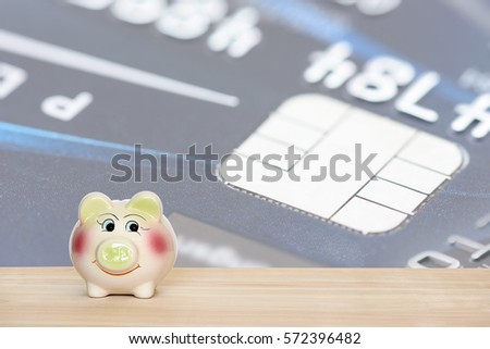 Ceramic piggy bank put on a wood table in front of a credit card microchip background. Ideas about saving money for paying off the future loans or debt from over spending. Financial concept.