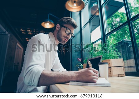 Yow angle view of a young stylish well dressed author writer is working in a modern coworking, writing the novel, in glasses, so serious and focused