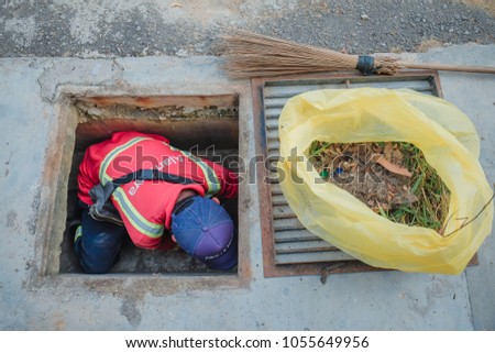 Muadzam Shah, Malaysia - March 22nd, 2018: Municipal worker "Alam Flora" uses sweepers and shovels to clean the garbage in the drain and put into the garbage bag.
