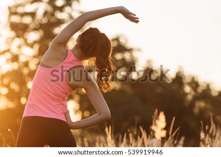 Young female stretching before fitness training session at the park. Healthy young woman warming up outdoors. She is stretching her arms and looking away,hi key.