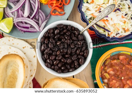 Top view of bowl with black beans, mini taco boats, cabbage, salsa - ingredients for taco with black beans and vegetables.