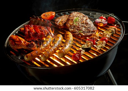 Assorted meat grilling over the hot fire on a portable barbecue with steak, sausage, kebabs, chicken , spare ribs and tomato