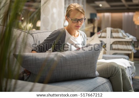 Pretty, young woman choosing the right furniture for her apartment in a modern home furnishings store (color toned image; shallow DOF)
