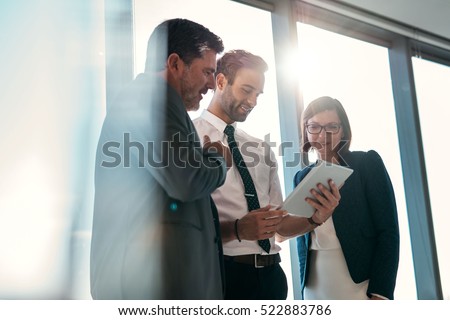 Group of businesspeople using a digital tablet together in front of office building windows overlooking the city