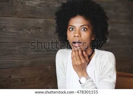 Human emotions and feelings. Close-up portrait of suprised African American female student with Afro haircut, shocked with results of exams, touching her chin and screaming, looking puzzled and scared