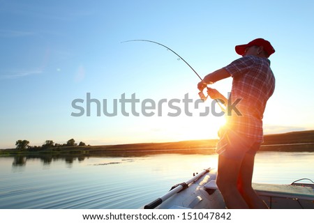 Young man fishing on a lake from the boat at sunset