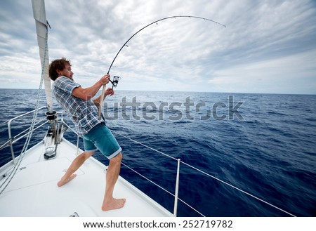 Young man fishing in open sea from sail boat