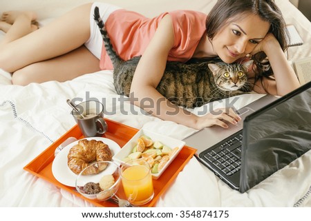 stock-photo-woman-watching-the-laptop-computer-and-having-breakfast-with-her-cat-on-bed-354874175.jpg