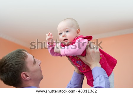 european young man holds his baby daughter above himself